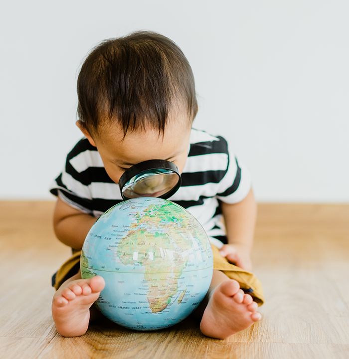 A boy holding a magnifying glass looking at a globe