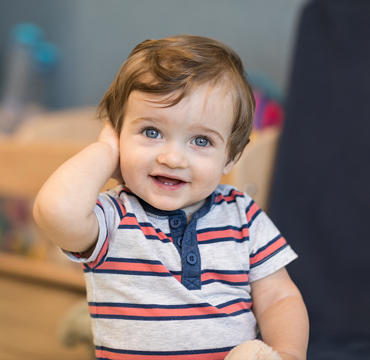 A little boy smiling with his hand covering his ear